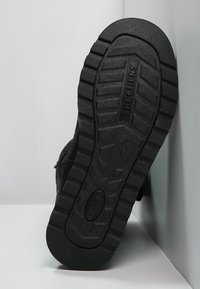 Czarna gumowa podeszwa z teksturowanym wzorem gripu; na śródstopiu znajduje się logo marki 'SKECHERS'. Widok z boku ukazuje sportowy styl designu.