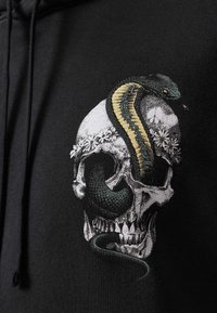 Hoodie noir avec un crâne brodé orné d'une couronne florale et d'un serpent vert, mettant en valeur des détails et textures complexes.