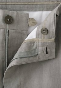 Gros plan de la taille d'un pantalon gris clair montrant un bouton, une boutonnière, une fermeture éclair partiellement ouverte et une doublure intérieure blanche.