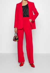 Czerwona dopasowana marynarka zestawiona z czerwonymi spodniami z wysokim stanem. Pod spodem czarna satynowa bluzka. Mała torebka w kratę i czerwone buty na obcasie.