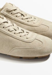 Vaaleanruskeat mokkasiinit matalalla profiililla, pyöristetyllä kärjellä ja teksturoidulla pinnalla. Mukana kudotut nauhat ja huomaamattomat ompelusaumat sivuilla.