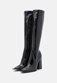 Bottes noires en cuir verni montant jusqu'au genou, avec un bout pointu et un talon épais. Texture lisse et détails minimalistes en métal.