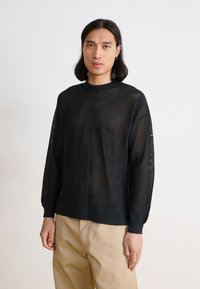Black knit sweater with a loose, open weave, ribbed cuffs, and hem. Features a crew neckline and slightly dropped shoulders.