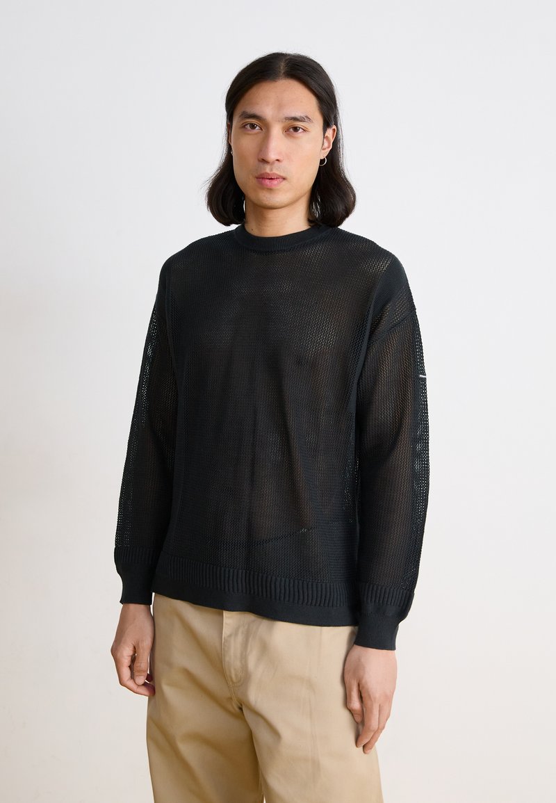 Black knit sweater with a loose, open weave, ribbed cuffs, and hem. Features a crew neckline and slightly dropped shoulders.