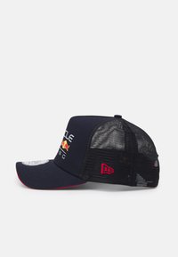 Mornarica kapa za bejzbol s čvrstim prednjim dijelom, mrežastim stražnjim dijelom, crvenim akcentima i dizajnom logotipa koji sadrži crvenog bika i tekst. Zakrivljeni vizir s detaljima šivanja.