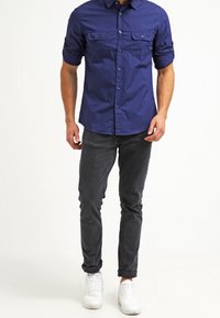 Marinblå skjorta med knappar och två bröstfickor, uppvikt ärmar, grå smal passform-byxor och vita sneakers. Mjuk tyg med en avslappnad design.