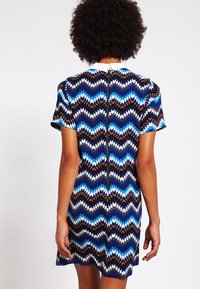 Vestido de manga corta con un patrón de zigzag multicolor en azul, blanco, marrón y negro, con una cremallera central en la parte posterior.