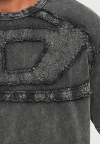 Černá džínová mikina s texturovaným, ošuntělým designem a abstraktním výřezem. Tkanina má mírně vybledlý vzhled.