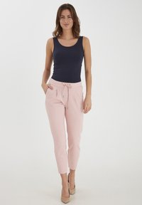Marineblauwe tanktop, lichtroze joggingbroek met zakken, taps toelopende silhoutte, zachte textuur, aangevuld met neutrale hakken.