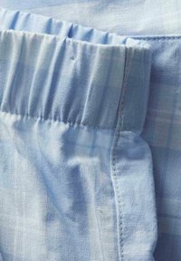 Gros plan d'une ceinture élastique bleu clair cousue à un tissu doux et tissé avec un motif à carreaux subtil.