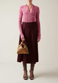 Top a maglia rosa con colletto, gonna plissettata bordeaux, calzini marroni a trama, e una borsa dorata con design a nodo e hardware circolare.