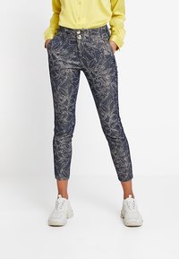 Housut merimieskuosisella valkoisella kukkakuviolla, lyhyet lahkeet, kaksi etutaskua ja kaksoispainonappi. Yhdistetty keltaiseen paitaan ja valkoisiin lenkkareihin.