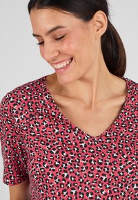Camiseta de cuello en V de color rosa con un estampado de leopardo en blanco y negro, mangas cortas y una textura de tela suave. Incluye un escote redondeado.