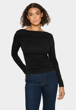 Black long-sleeve top with off-the-shoulder design, gathered texture at front, paired with dark blue jeans. Smooth fabric and fitted shape.