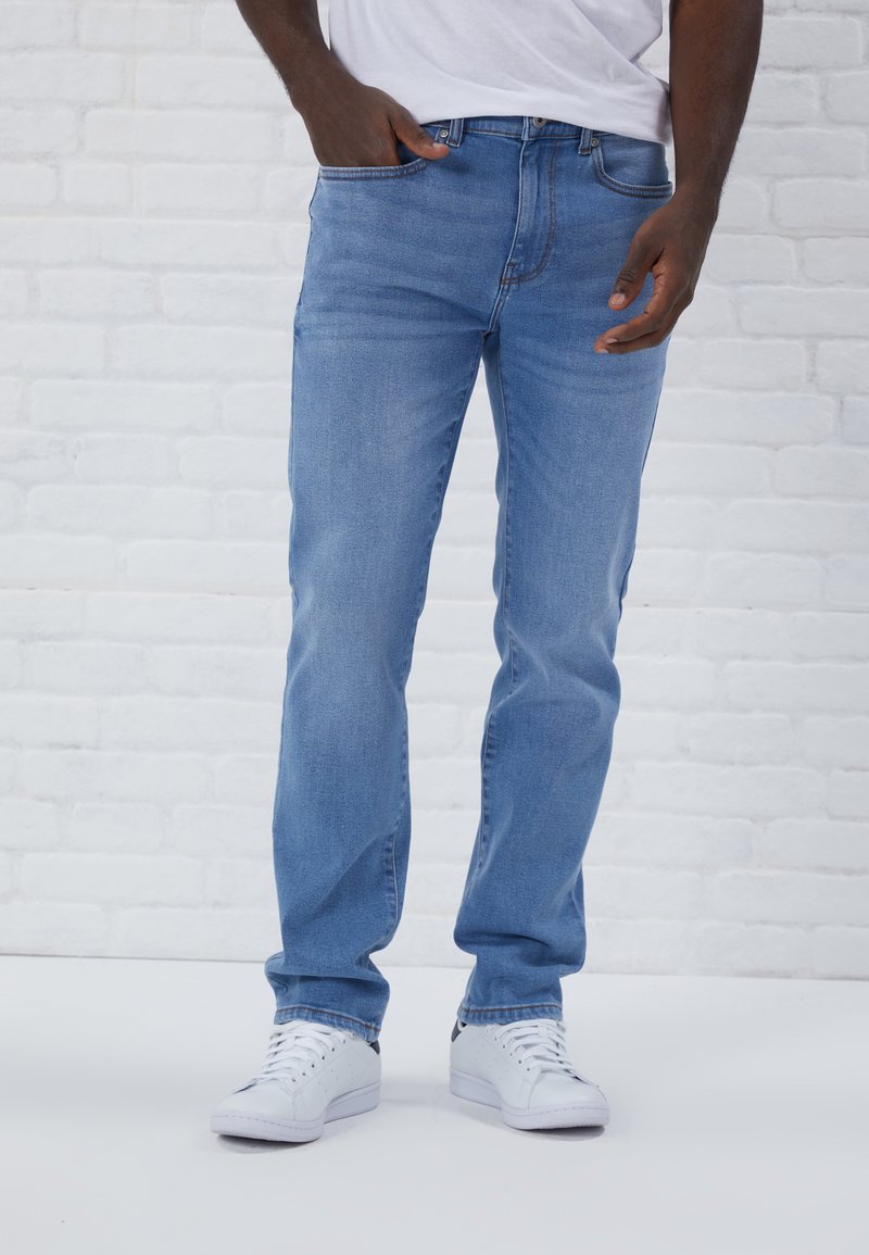 Light blue denim jeans with a straight leg fit, five-pocket design, and subtle stitching details, paired with white sneakers.