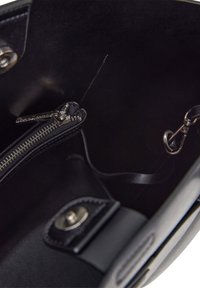 Interno di una borsa in pelle nera con una tasca con zip e una texture liscia. Presenta hardware in metallo e una tracolla rimovibile.