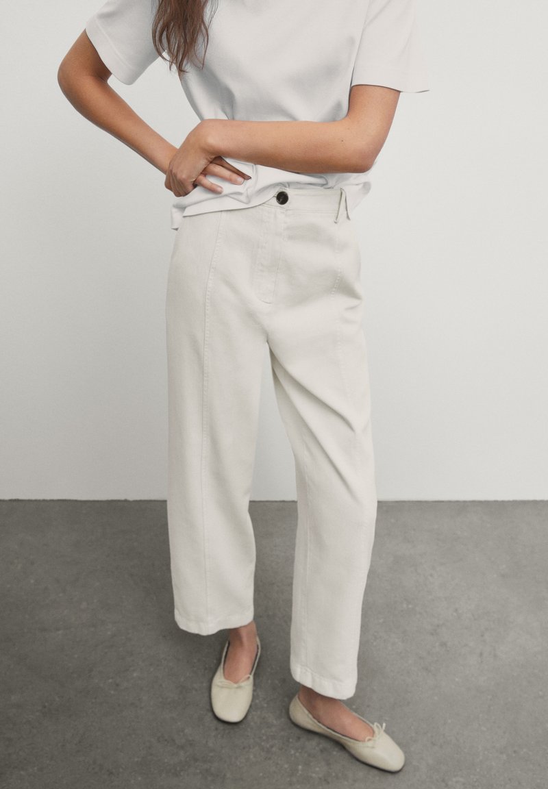 High-waisted, wide-leg trousers in light beige denim, featuring front pockets and a button closure, paired with a simple grey T-shirt.