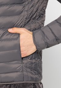 Grå isoleret jakke med vandret quiltet mønster, med sidelomme og elastiske ærmegab for en tæt pasform. Glat, letvægtsstof.