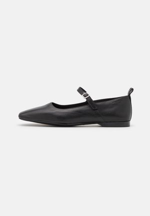 Chaussure plate Mary Jane en cuir noir avec bout pointu, petite bride à boucle et petit talon sur fond blanc.