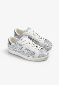 Sneakers pokryte brokatem z srebrnym akcentem, beżowymi sznurowadłami i teksturowaną, off-white podeszwą. Zawierają detal w postaci czaszki i skrzyżowanej kości na boku.