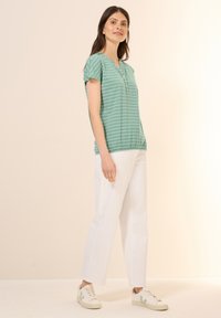 Haut à rayures turquoise à manches courtes avec un col rond et une patte de boutonnage, associé à un pantalon droit blanc et des baskets beiges.