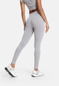 Szare legginsy z elastycznego materiału, z wysokim stanem i dopasowanym krojem. Noszone z białymi trampkami, pokazujące gładką fakturę.