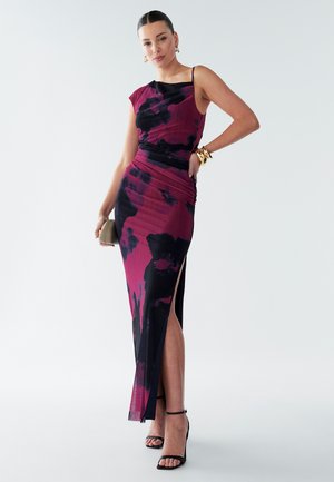 Dopasowana sukienka bez rękawów w kolorze czarnym i głębokim różowym z kwiatowym wzorem, z rozcięciem po boku i marszczoną talią. Akcesoria obejmują kolczyki koła i kopertówkę.