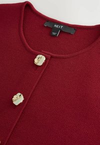 Bordeaux gebreide cardigan met een ronde halslijn, voorzien van vier decoratieve knopen in goudkleur en een textuurstofafwerking. Merketiket zichtbaar.