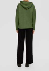Groene hoodie met een ontspannen pasvorm, geribbelde zoom en zijnaden, gecombineerd met zwarte broek met brede pijpen en stevige zwarte schoenen.