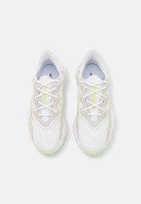 Pair of white and light gray Adidas sneakers with neon yellow accents and white laces, viewed from the top on a white background.