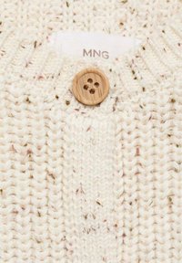 Pull en crème tricoté avec un motif texturé, présentant un bouton en bois et de légers éclats dans des nuances de marron et de vert. L'étiquette indique "MNG".
