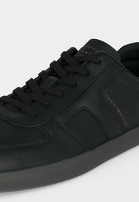 Baskets en cuir noir Tommy Hilfiger avec lacets noirs et texte doré de marque sur le côté et la languette, montrant les détails avant et latéraux.