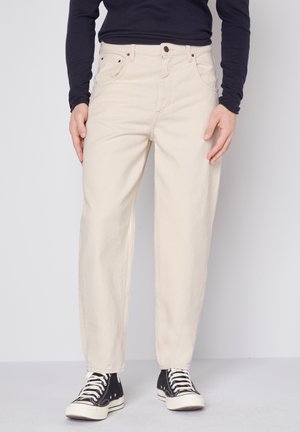 Jeans en coton beige à coupe droite, cinq poches et quincaillerie argentée. Associés à des baskets montantes noires avec des semelles blanches.