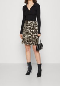 Svart långärmad topp med en notched krage, i kombination med en knälång beige kjol med svart prickmönster och volangkanter. Svarta ankelstövlar.