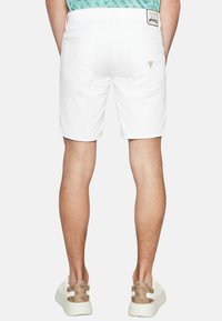 Shorts in denim bianco con taglio dritto, tasche posteriori e una discreta etichetta con il marchio sulla cintura. Indossati con sneakers bianche.