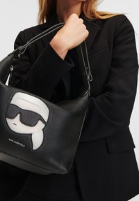 Sort læder taske med struktureret overflade; prydet med en hvid og sort Karl Lagerfeld karakter iført solbriller; justerbar skulderrem.