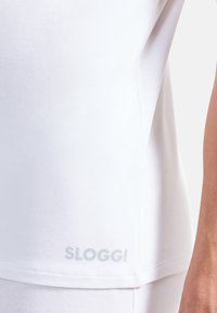 Weißes T-Shirt mit einer weichen, glatten Textur, das am Saum ein dezentes graues Logo zeigt, mit einem lässigen Schnitt und kurzen Ärmeln.