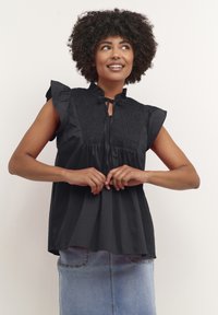 Bluză neagră cu mâneci scurte, cu bust elastic și mâneci volă, având un decolteu cu deschidere și o croială confortabilă. Asortată cu o fustă din denim.