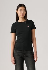 T-shirt noir à col rond en coton, avec des manches courtes et un petit logo rouge Levi's sur la poitrine gauche. Tissu texturé.