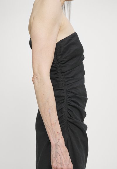Black strapless dress with a ruched design on the side. The fabric appears soft with a smooth texture. Shown on a model from the side.