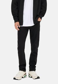 Czarne spodnie jeansowe o wąskim kroju, zestawione z białym T-shirtem i czarną bluzą z kapturem na suwak, uzupełnione masywnymi białymi sneakersami z zielonymi akcentami.