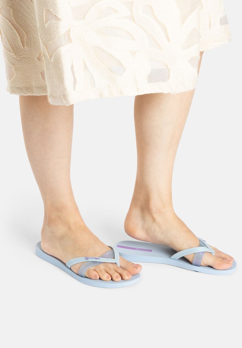 Light blue flip-flops feature a soft, textured footbed, thin straps with a slightly glittery finish, and a simple, modern design.