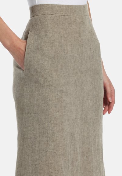 Woman wearing high-waist beige linen skirt with side pockets, one hand in pocket and the other resting by side.