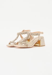 Beige sandály na řemínky s dekorativními rhinestones, polstrovanou stélkou a blokovým podpatkem se zlatými akcenty. Hladký svrchní materiál.