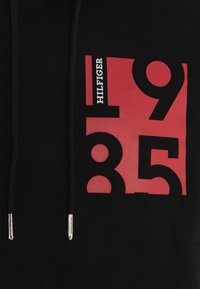 Felpa nera con cappuccio caratterizzata da una grande grafica rossa con i numeri "1935" e "HILFIGER" stampati in bianco. Include terminali metallici argentati sui lacci.