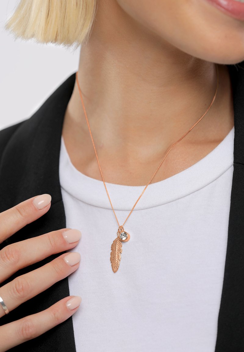 Roosakullast kaelakee sulgkujuline ripats ja väike ümmargune kristall. Kandmisel valge särke all ja musta bleiseri all.