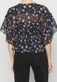 Blusa nera trasparente con stampa floreale in viola e bianco. Presenta maniche arricciate e un elastico in vita, creando una vestibilità ampia.