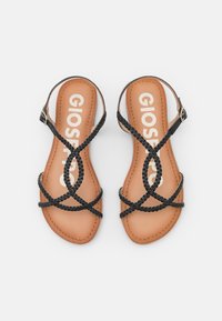 Mustat punotut sandaalit, joissa on ristikkäiset hihnat ja vaaleanruskea nahkainen pohja. Varustettu soljella ja yksinkertaisella, minimalistisella suunnittelulla.