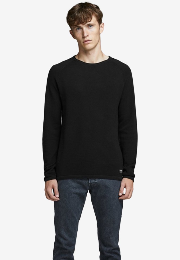 Schwarzer Rundhalsausschnitt-Pullover aus weichem Stoff, mit langen Ärmeln und geradem Saum. Kombiniert mit dunklen Jeans. Minimalistisches Design.