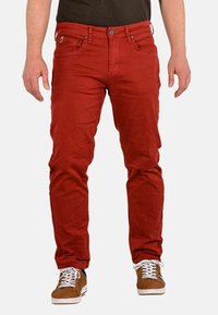 Jeans rojos ajustados con cinco bolsillos, botón de metal y costuras tonales. El material parece ligeramente texturizado y tiene un aspecto casual y desgastado.
